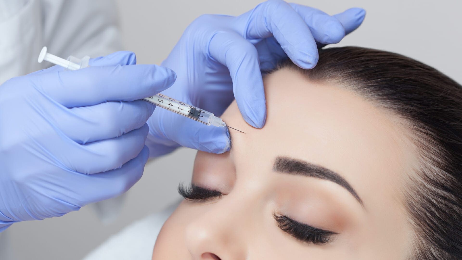 A cosmetologist gives a facial botox injection for tightening and smoothing wrinkles on the face and skin of a beautiful young woman in a skin clinic.